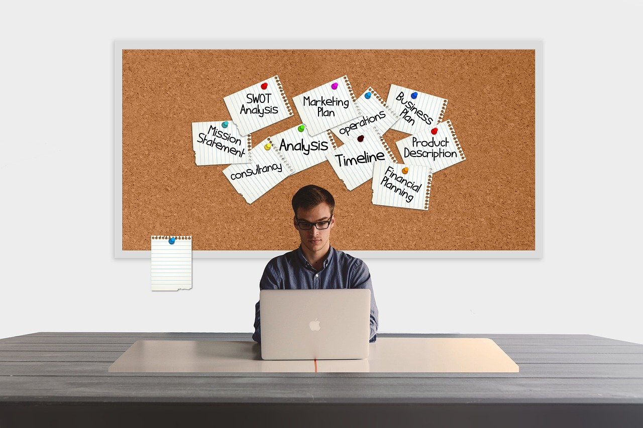 man working on laptop, bulletin board with stickie notes