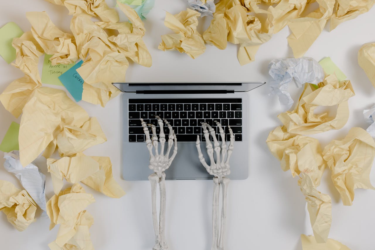 Crumpled papers beside a skeleton operated laptop-relates to Should We Work 14 Hours a Day? A Double-Edged Sword